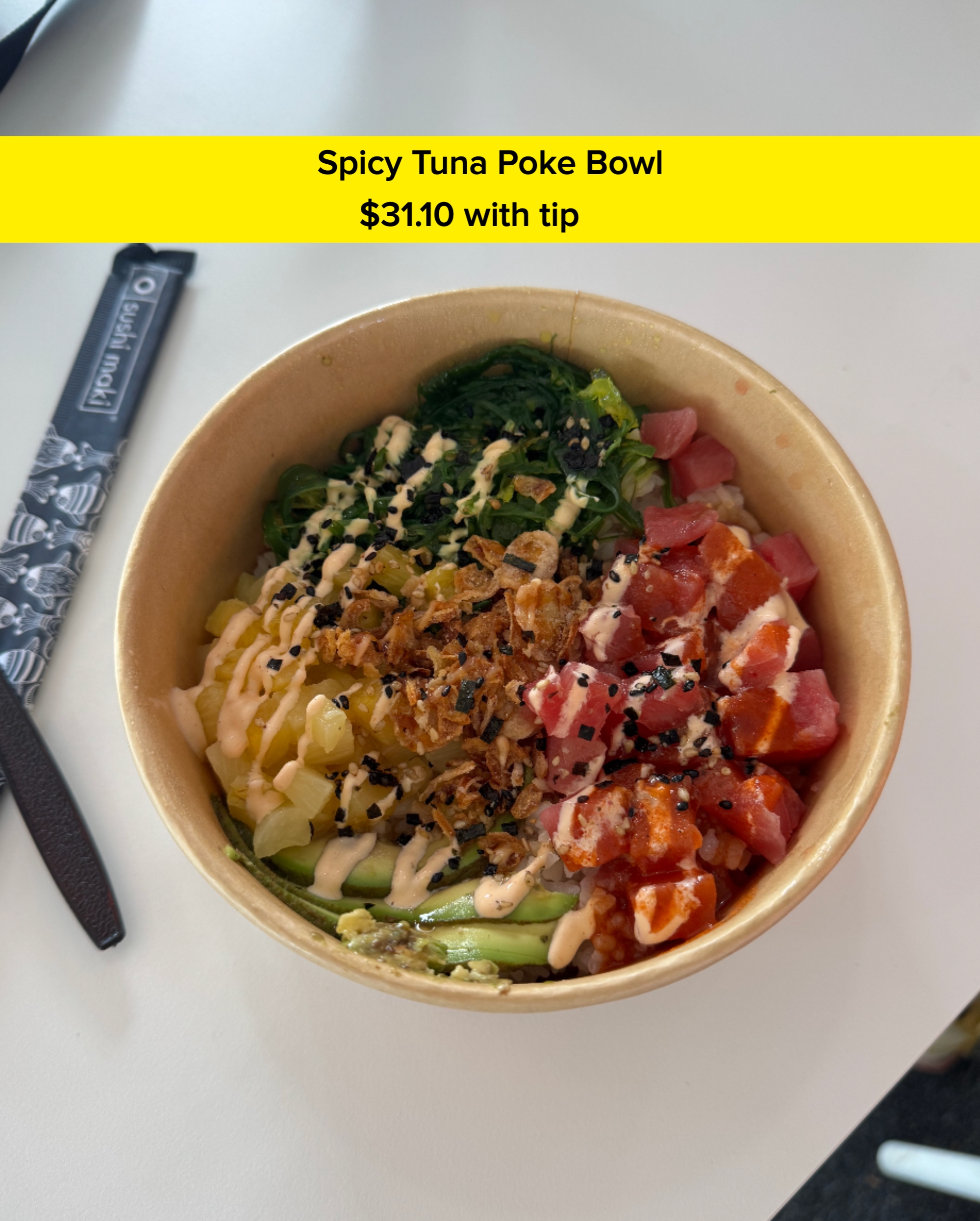 A bowl of poke with tuna, salmon, avocado, seaweed, and toppings on a white surface, with a black chopstick and napkin beside it