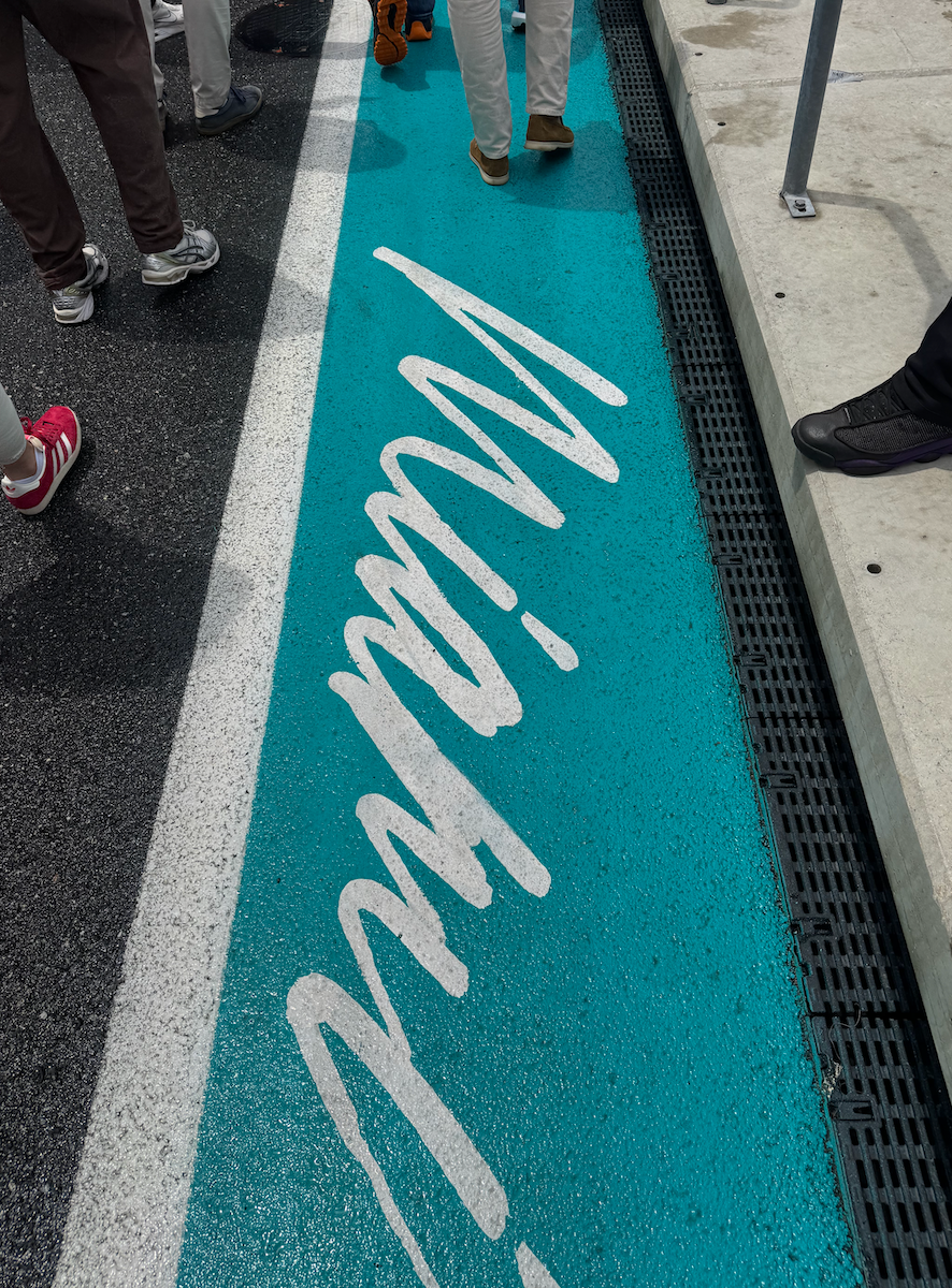People walking on a blue path with "Miami" written in script, likely at a race track or event venue