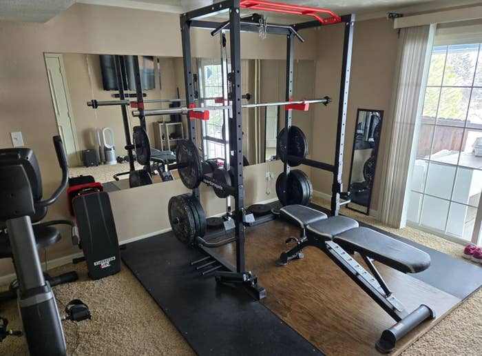 Home gym setup with a weight rack, bench, and various weights in a room, shared on a Reddit page about budget-friendly home gyms