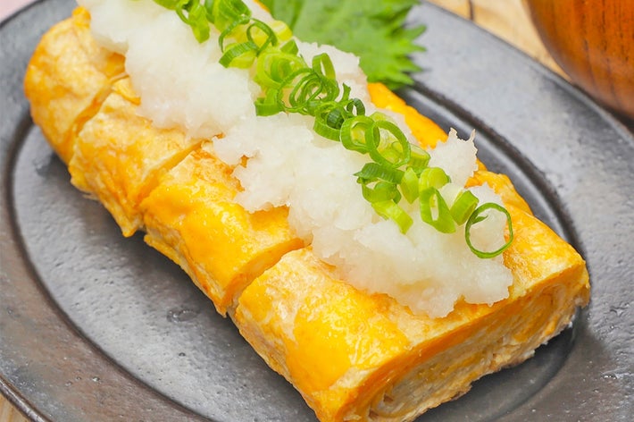 卵焼きに大根おろしとネギが添えられた和風料理が黒い皿に盛られている。