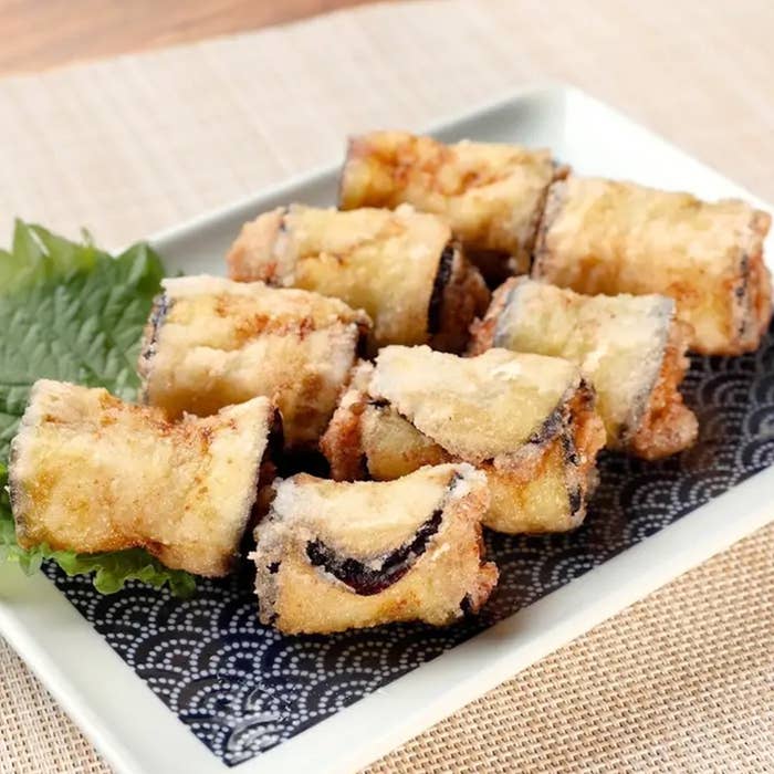 皿に盛られた揚げナスの天ぷら。背景に大葉が添えられ、食欲をそそる見た目。