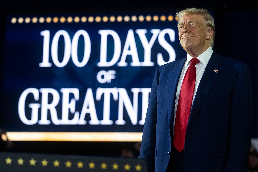 A person stands confidently in front of a large sign reading "100 Days of Greatness."
