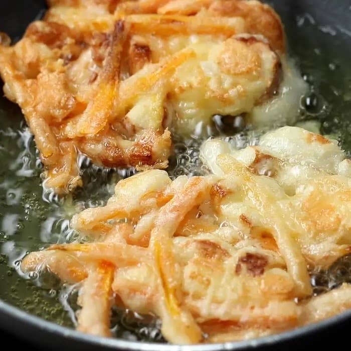 フライパンで揚げているかき揚げの様子。細切りの野菜が衣でまとわれている。