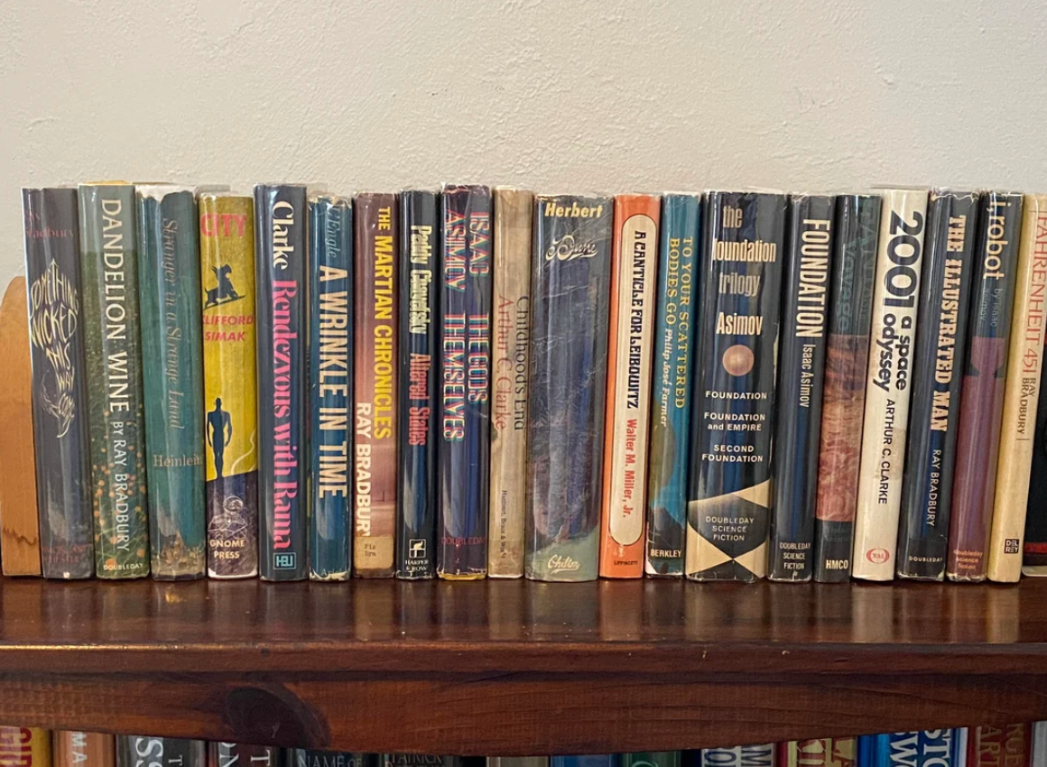 A bookshelf lined with classic science fiction books, including works by Ray Bradbury, Isaac Asimov, Arthur C. Clarke, and Herbert