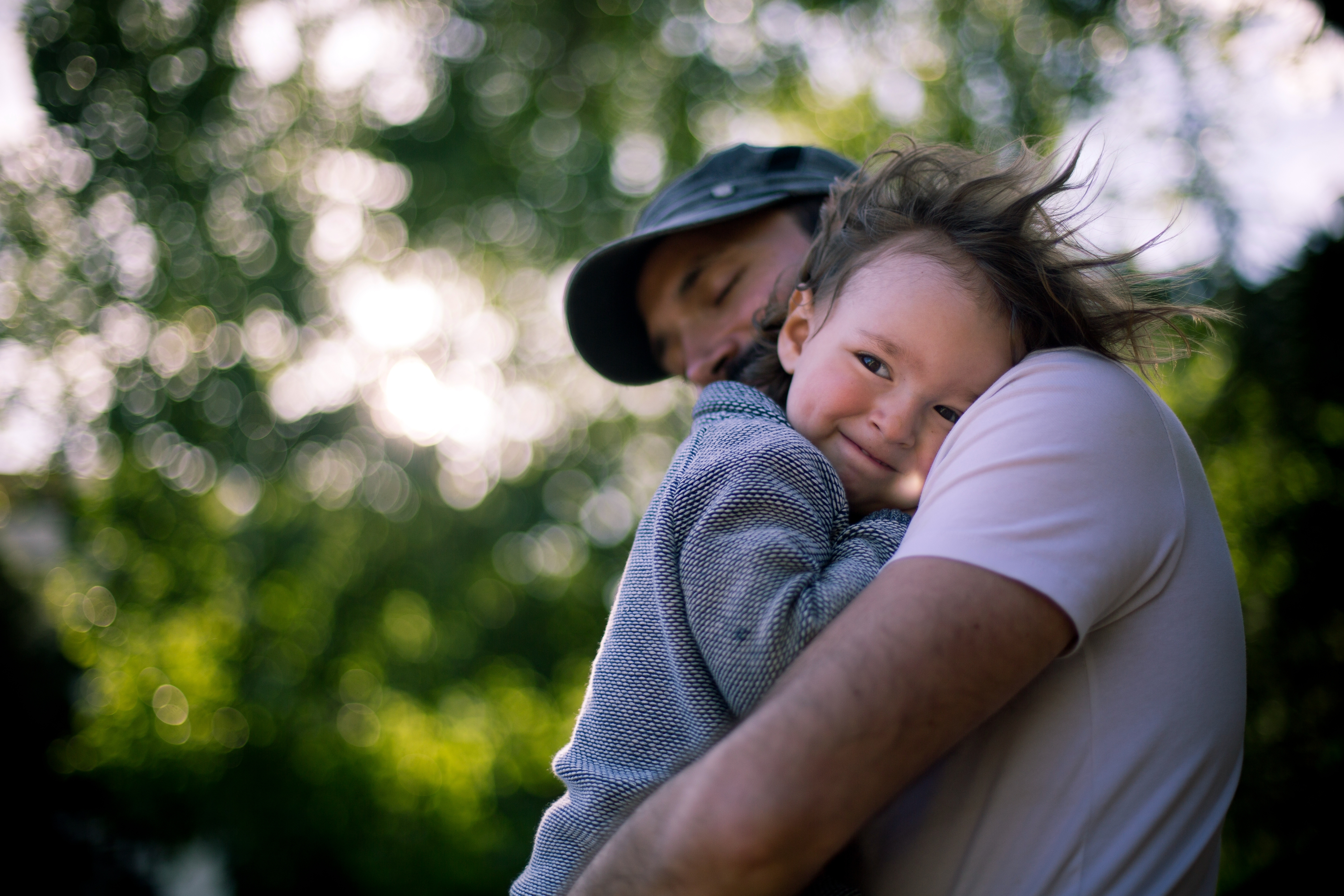 A person embraces a smiling child outdoors, with blurred trees in the background, creating a warm, serene atmosphere