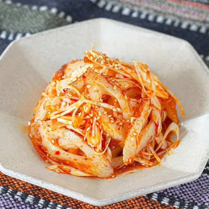 白い皿に盛り付けられた、辛そうな調味料で和えられたエリンギとエノキの料理。ゴマがかかっている。