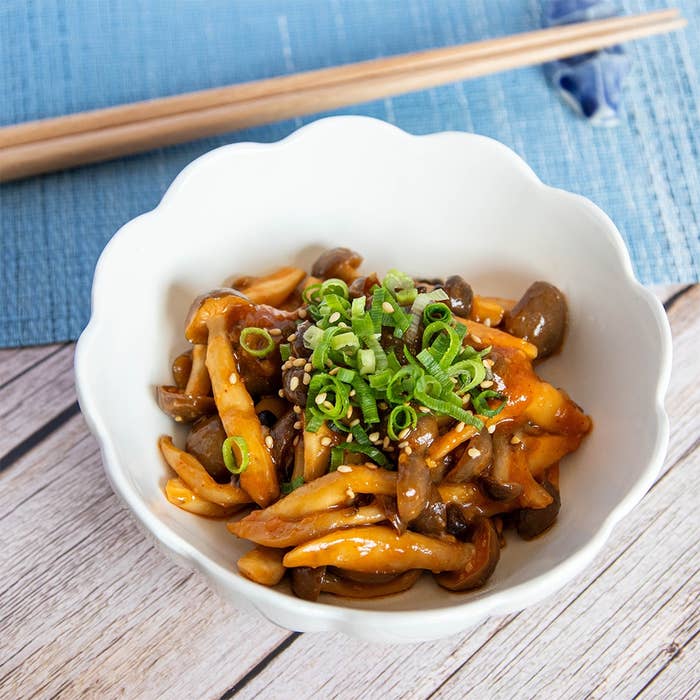 白い器に盛られた、きのことネギ、ゴマがのった料理。背景には青いランチョンマットと箸がある。