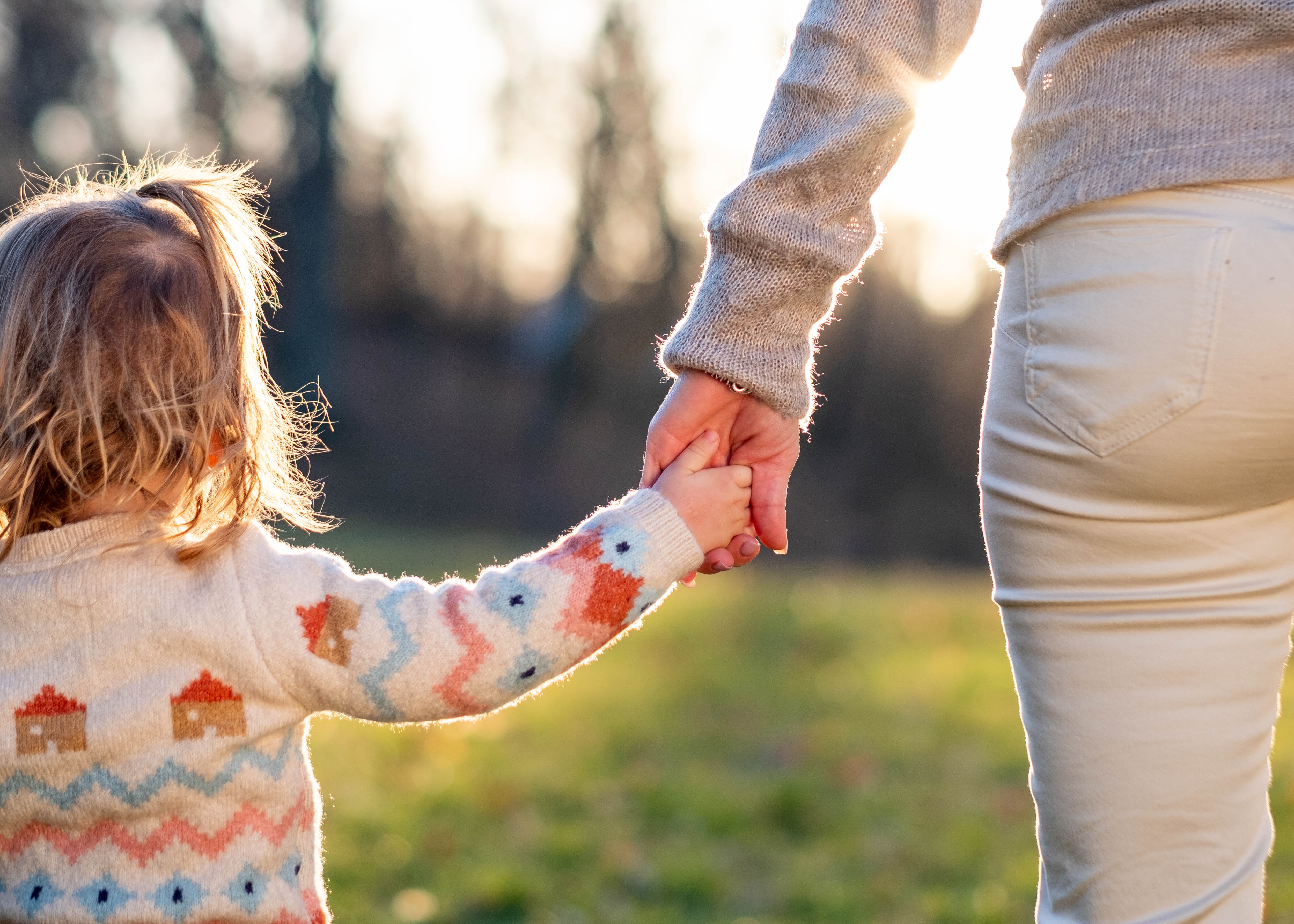 Child and adult holding hands outside.