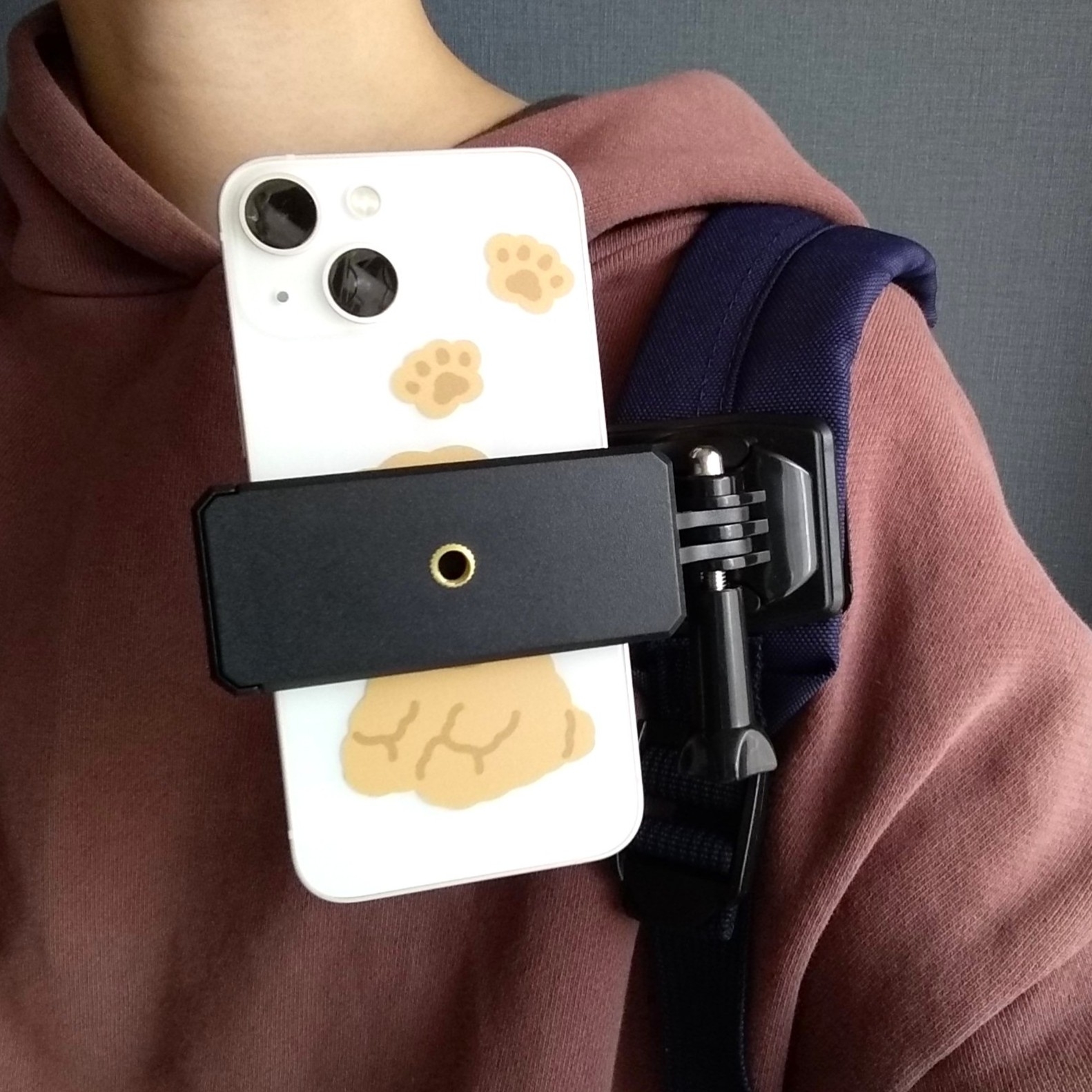 スマートフォンが肩に固定されたホルダーに装着されている画像。電話の背面に動物の足跡のデザインがあります。