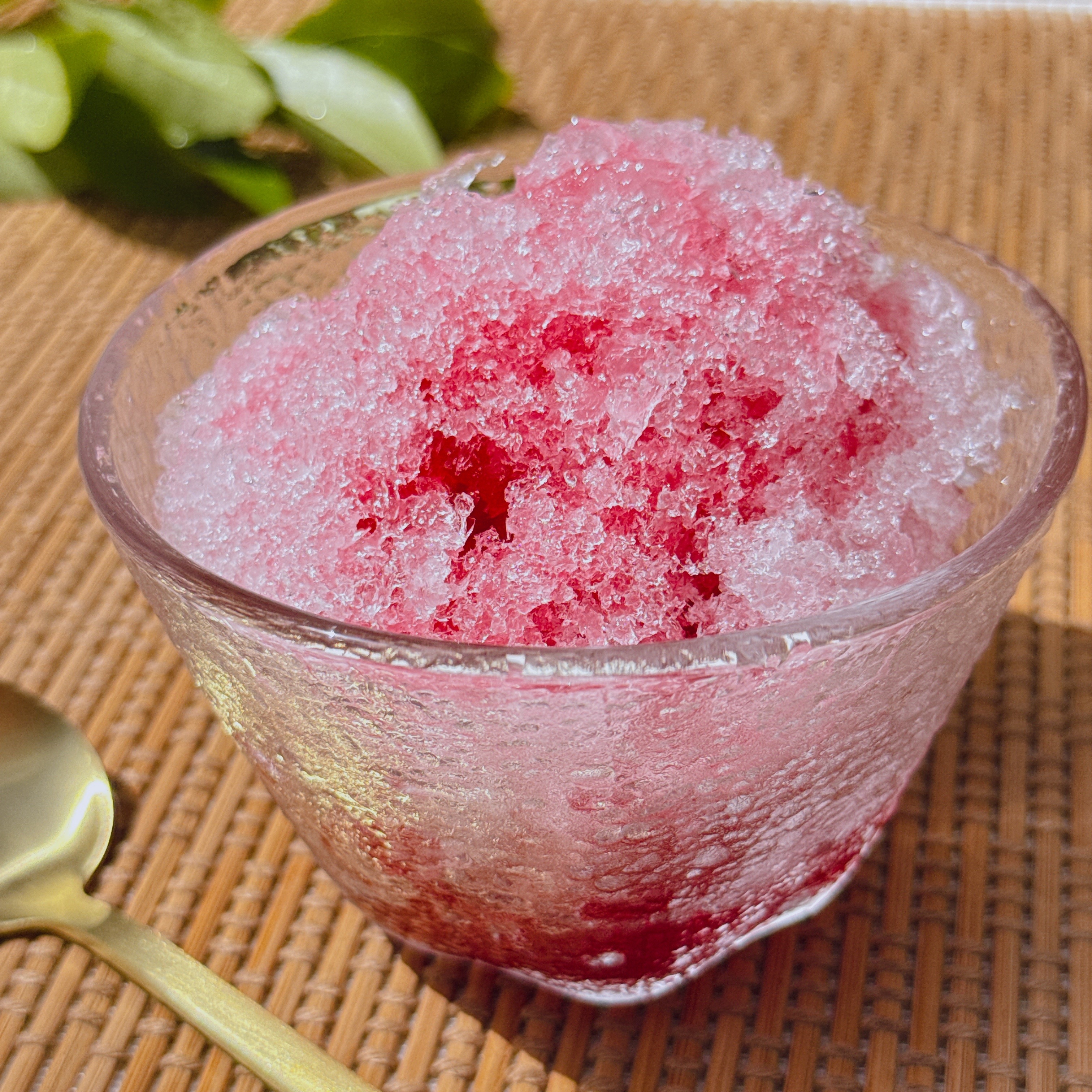 かき氷が透明なグラスに盛られています。隣に金色のスプーンが置かれています。