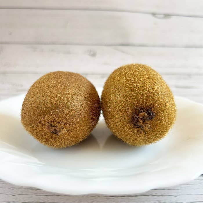 白い皿に乗った2つのキウイフルーツ。背景は木目調の壁。