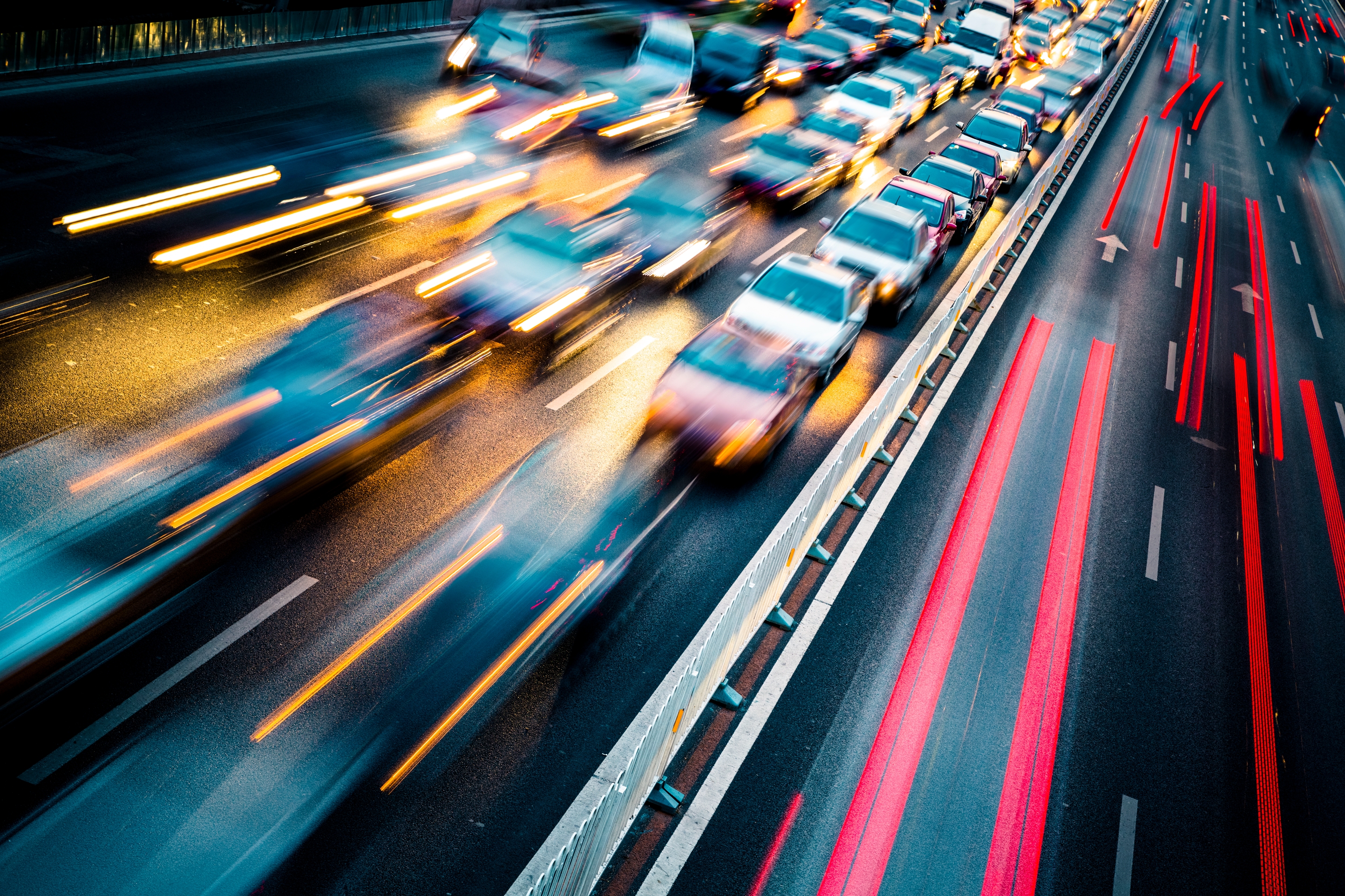 Blurred view of a busy highway with moving car lights creating dynamic streaks, showcasing fast-paced urban traffic at night.