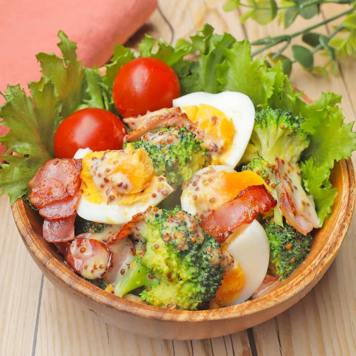 野菜サラダのボウルに、ゆで卵、ブロッコリー、トマト、ベーコン、葉野菜が盛り付けられている。
