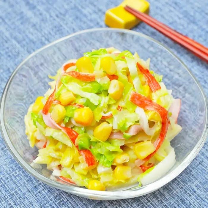 ガラスのボウルに盛られたサラダ。キャベツ、カニカマ、コーン、ハムのスライスが混ぜ合わされている。