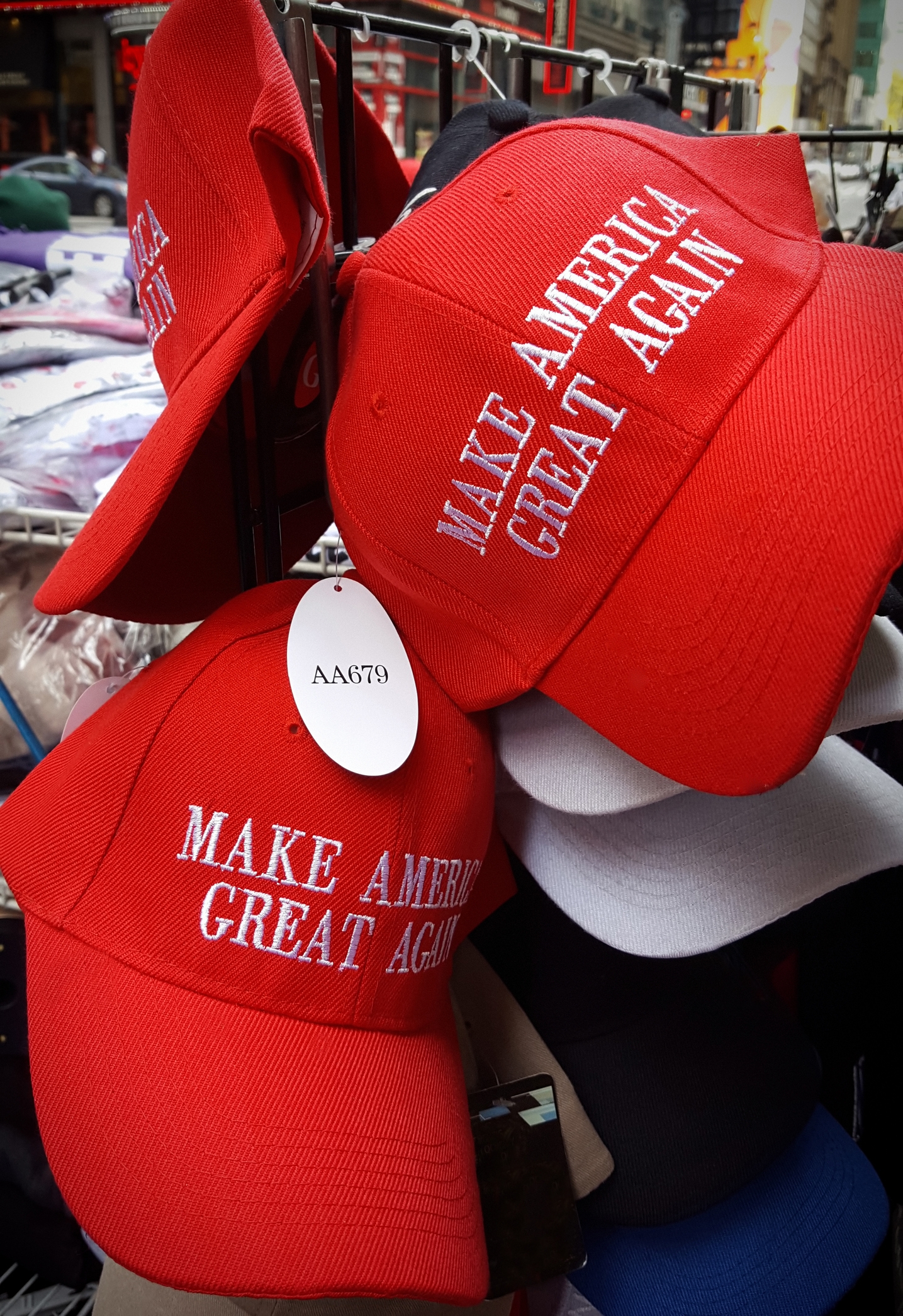 Red caps with "Make America Great Again" text embroidered on them displayed for sale. Tags attached, indicating product code AA679