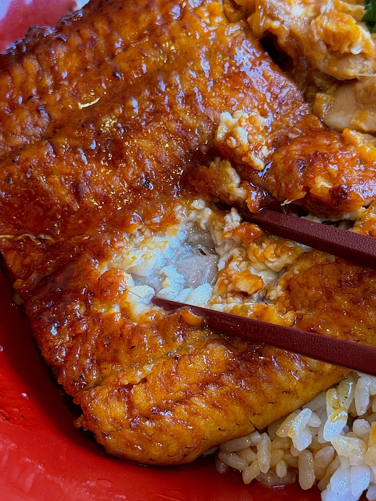 Close-up of grilled eel on rice, held by chopsticks