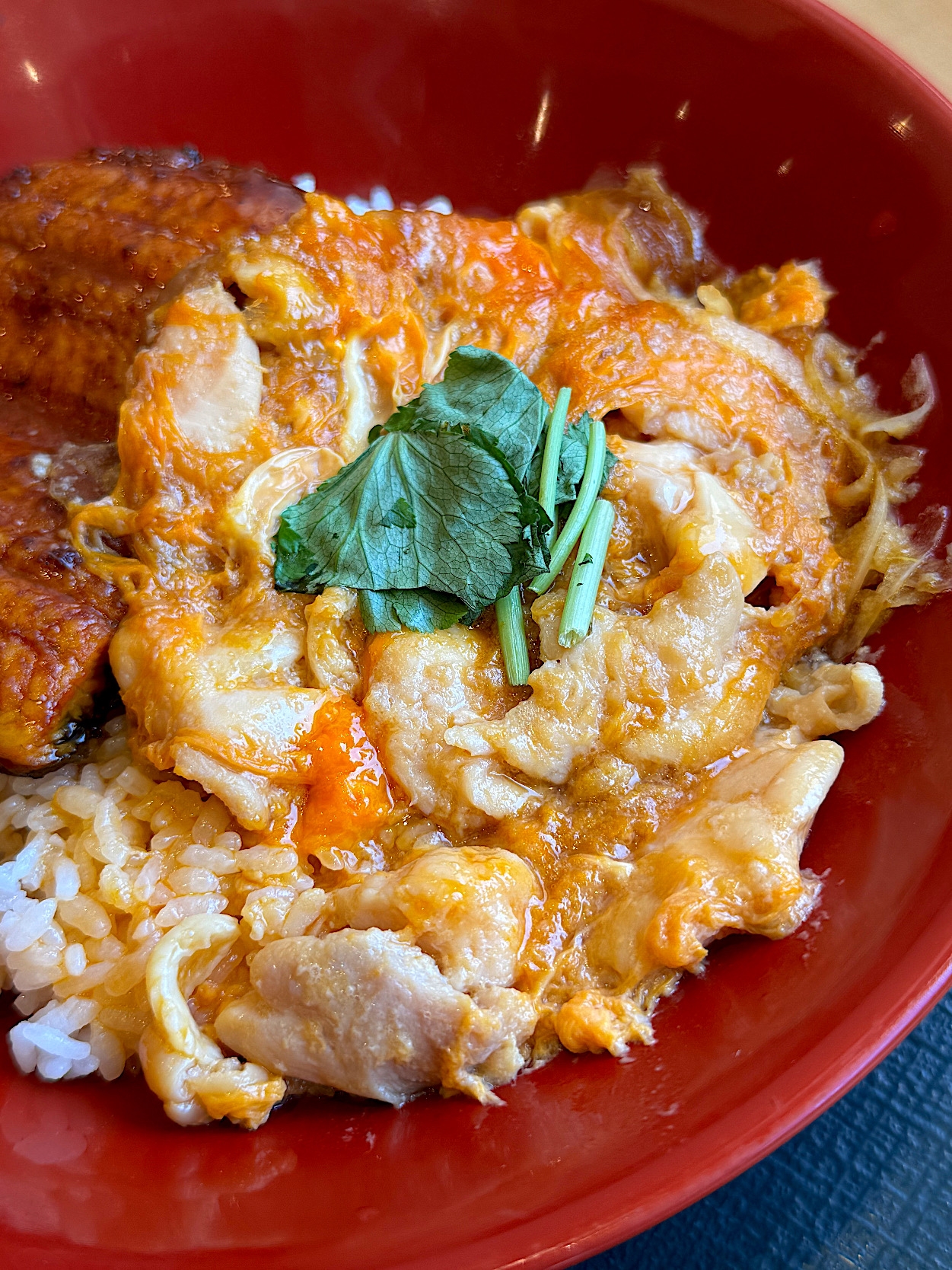 A bowl of rice topped with cooked egg and chicken, garnished with parsley on top