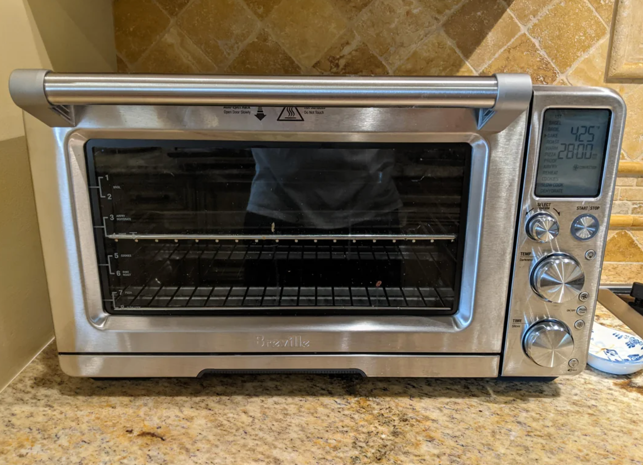 A kitchen counter with a Breville toaster oven, displaying control knobs and a transparent door. A Reddit thread above asks for baking tips with this oven