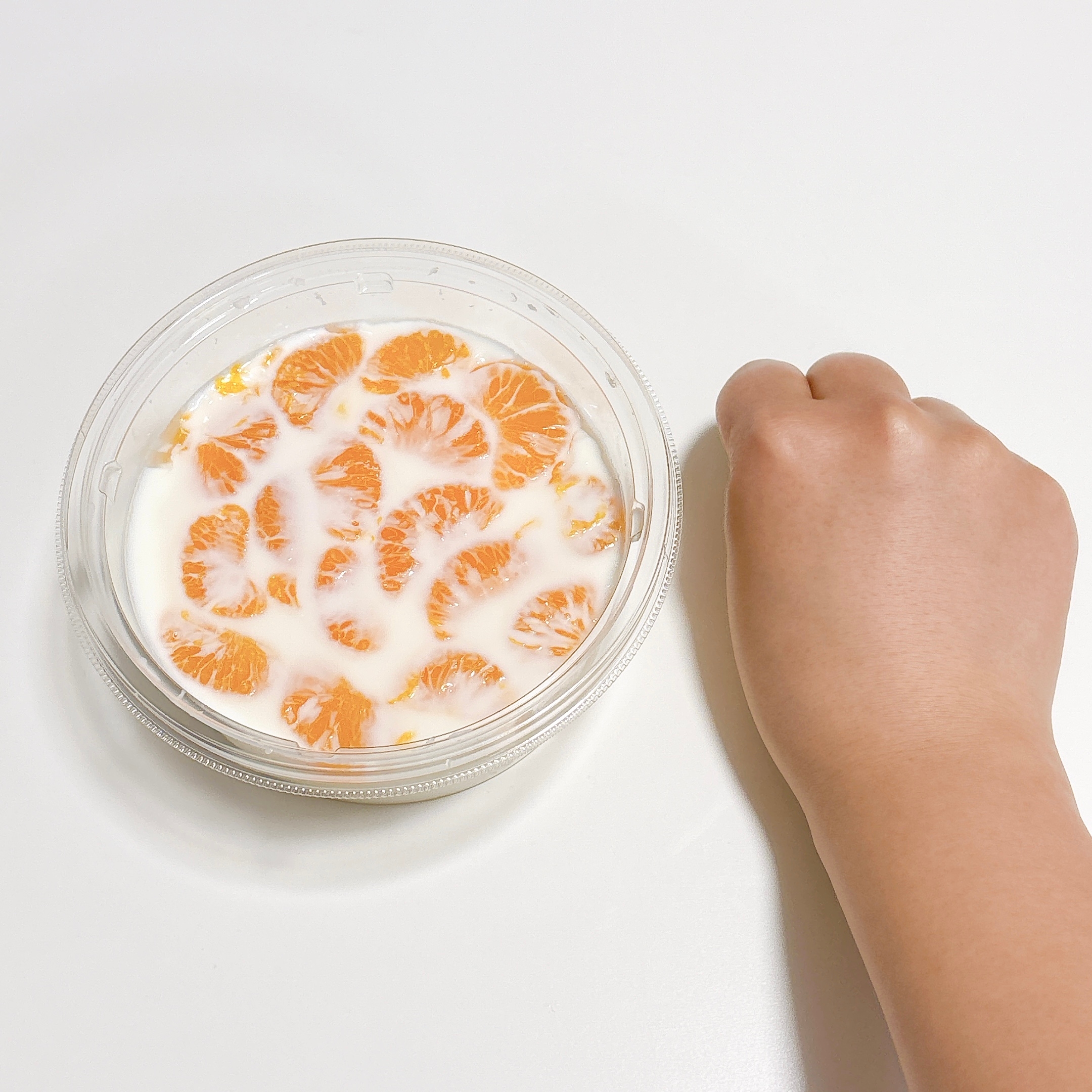 手の横に置かれた容器に、みかんとヨーグルトが入っている。