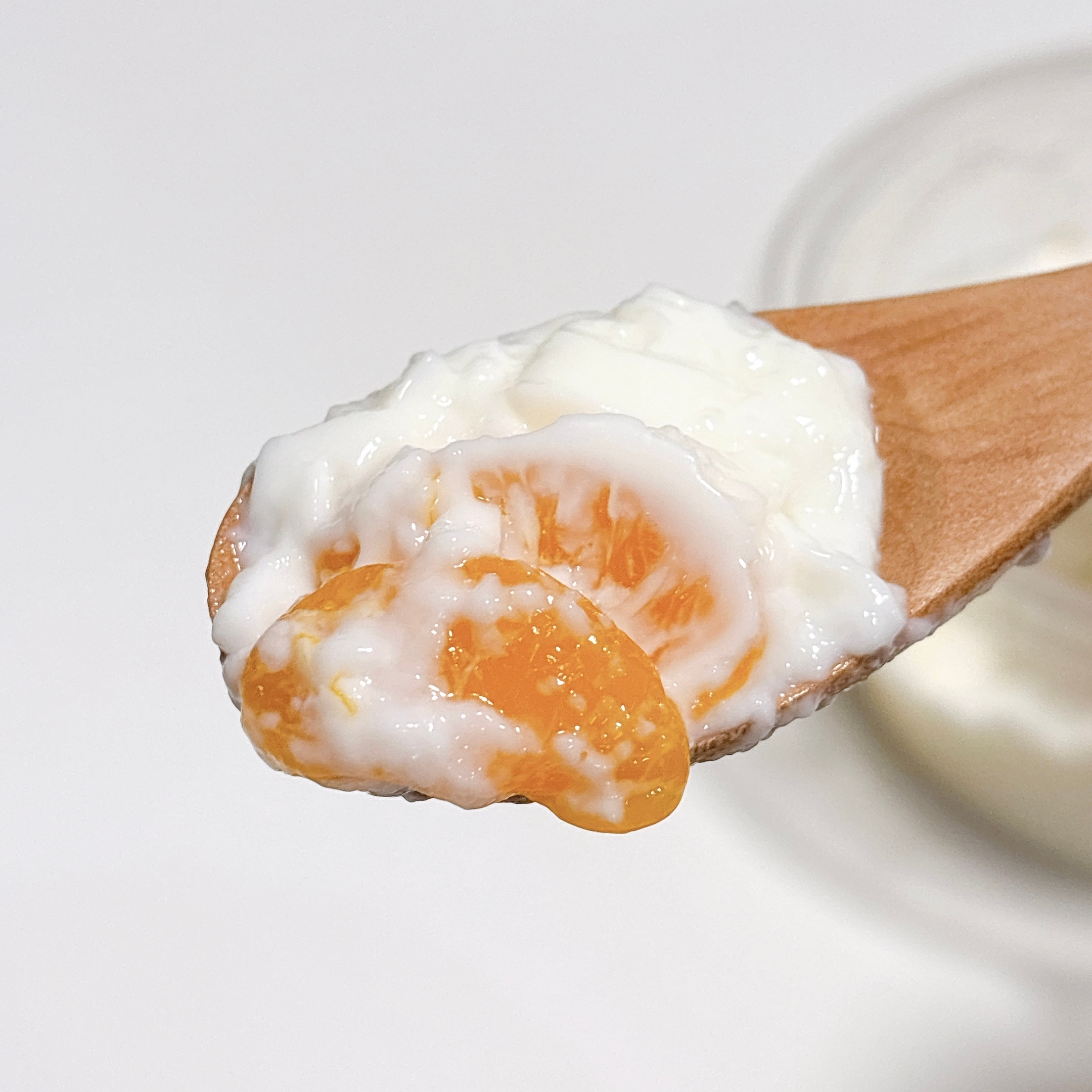 木製スプーンにヨーグルトとオレンジの果肉が載っている。