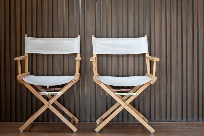 Two wooden director chairs with white canvas seats are positioned side by side in front of a striped background