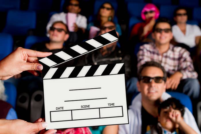 Audience wearing 3D glasses in a theater while a clapperboard is held up in the foreground