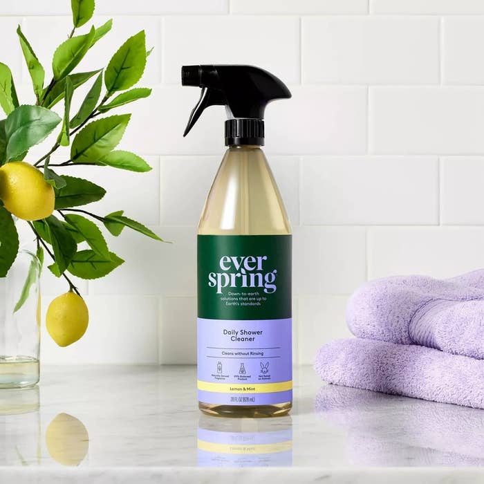 A vessel  of Everspring Daily Shower Cleaner with lemons connected  a subdivision  and purple towels successful  the background, acceptable   against a achromatic  tiled wall
