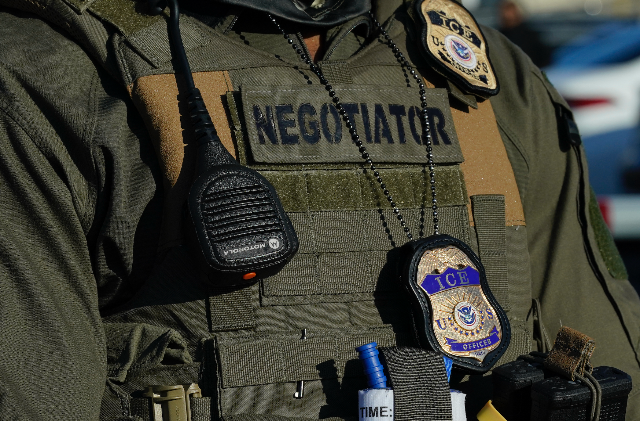 Close-up of a tactical vest with a "NEGOTIATOR" patch, radio, and two badges