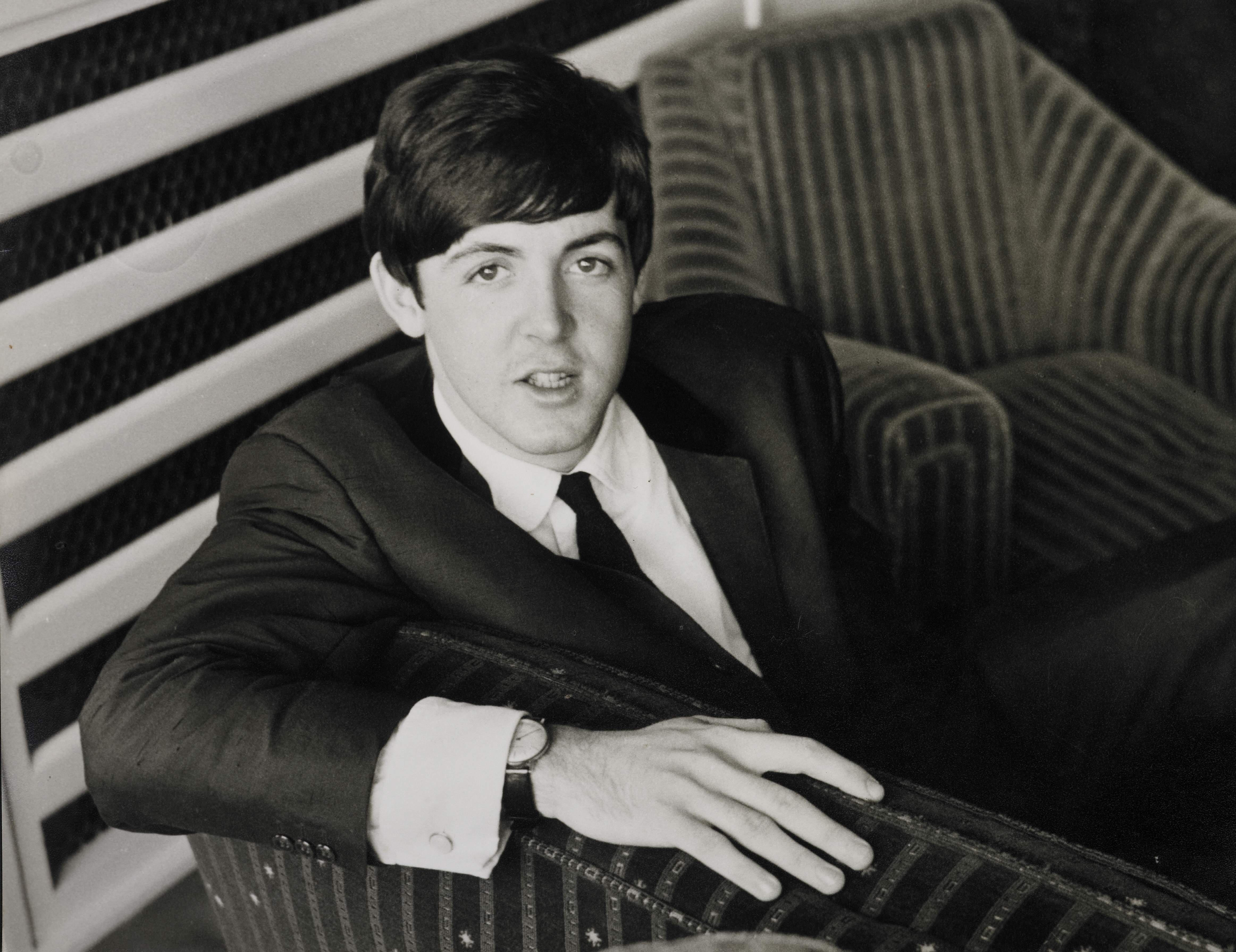 A person in a classic suit sits on a striped sofa, looking at the camera with a relaxed expression