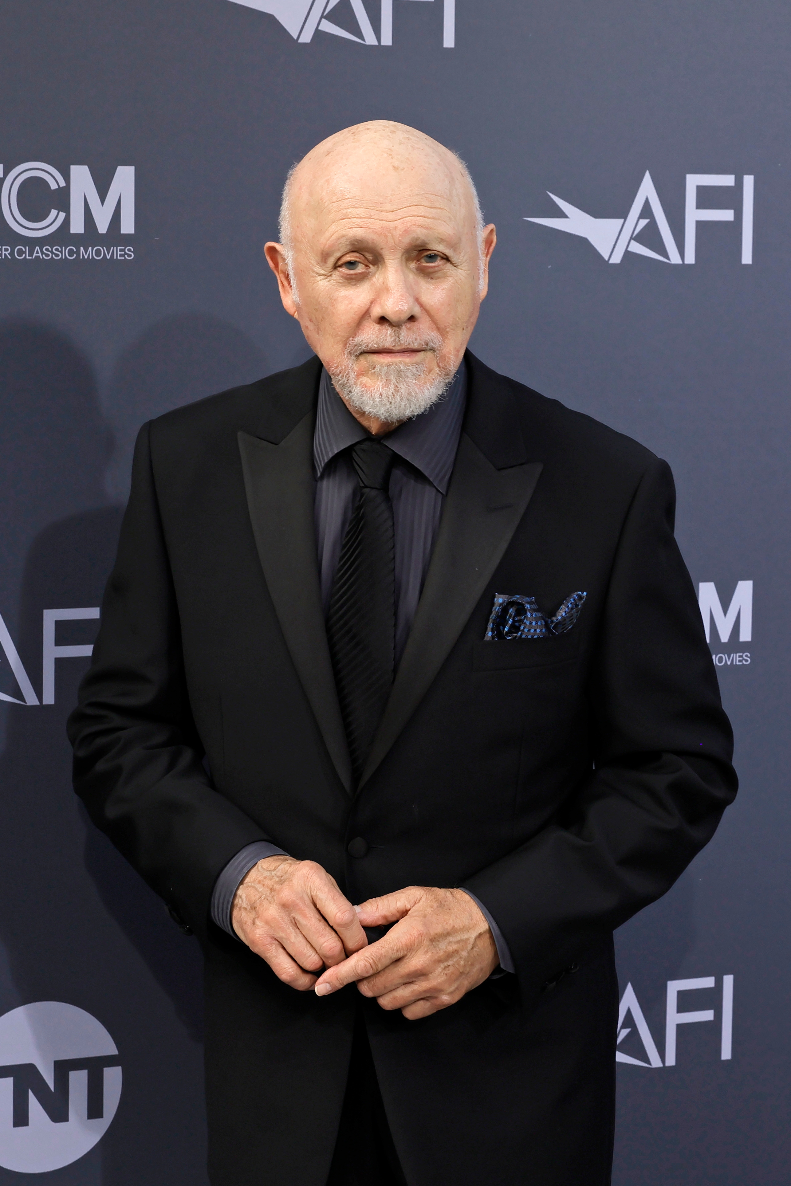 An individual stands on a red carpet in a black suit with a patterned pocket square, posing at an event with AFI branding