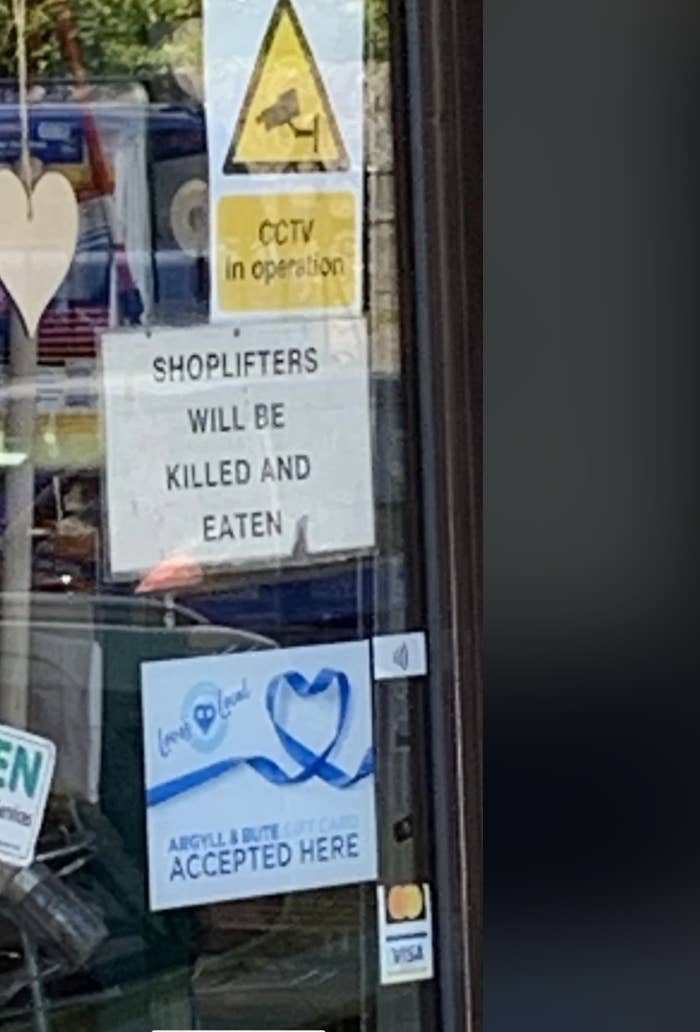 Storefront sign humorously warns: "Shoplifters will be killed and eaten." CCTV notice and payment method stickers also visible