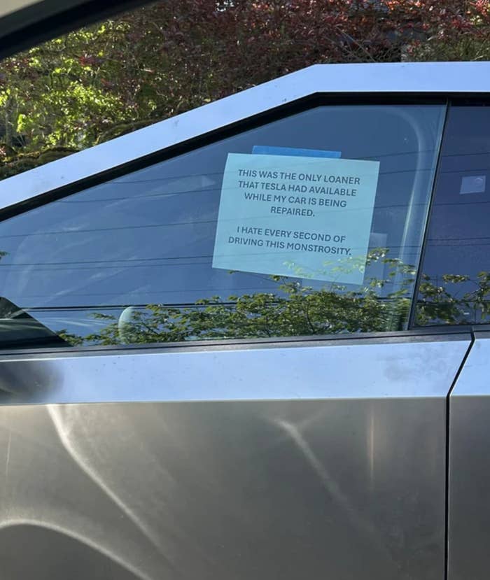 Sign on car reads: "This was the only loaner that Tesla had available while my car is being repaired. I hate every second of driving this monstrosity."