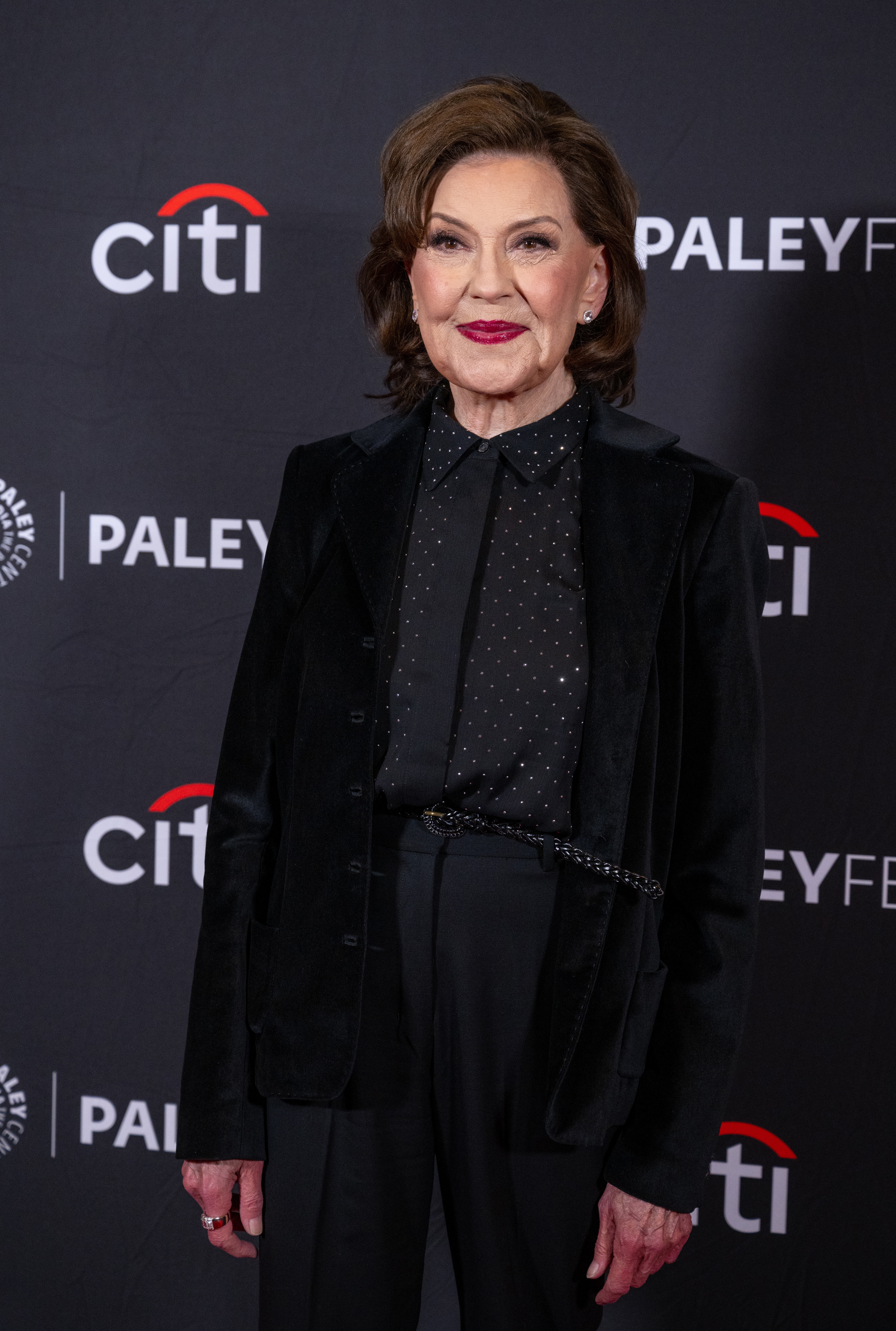 Woman on red carpet in black blazer with subtle dotted shirt at PaleyFest event backdrop