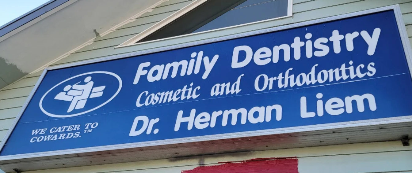 Sign for "Family Dentistry: Cosmetic and Orthodontics, Dr. Herman Liem" with the tagline "We cater to cowards."