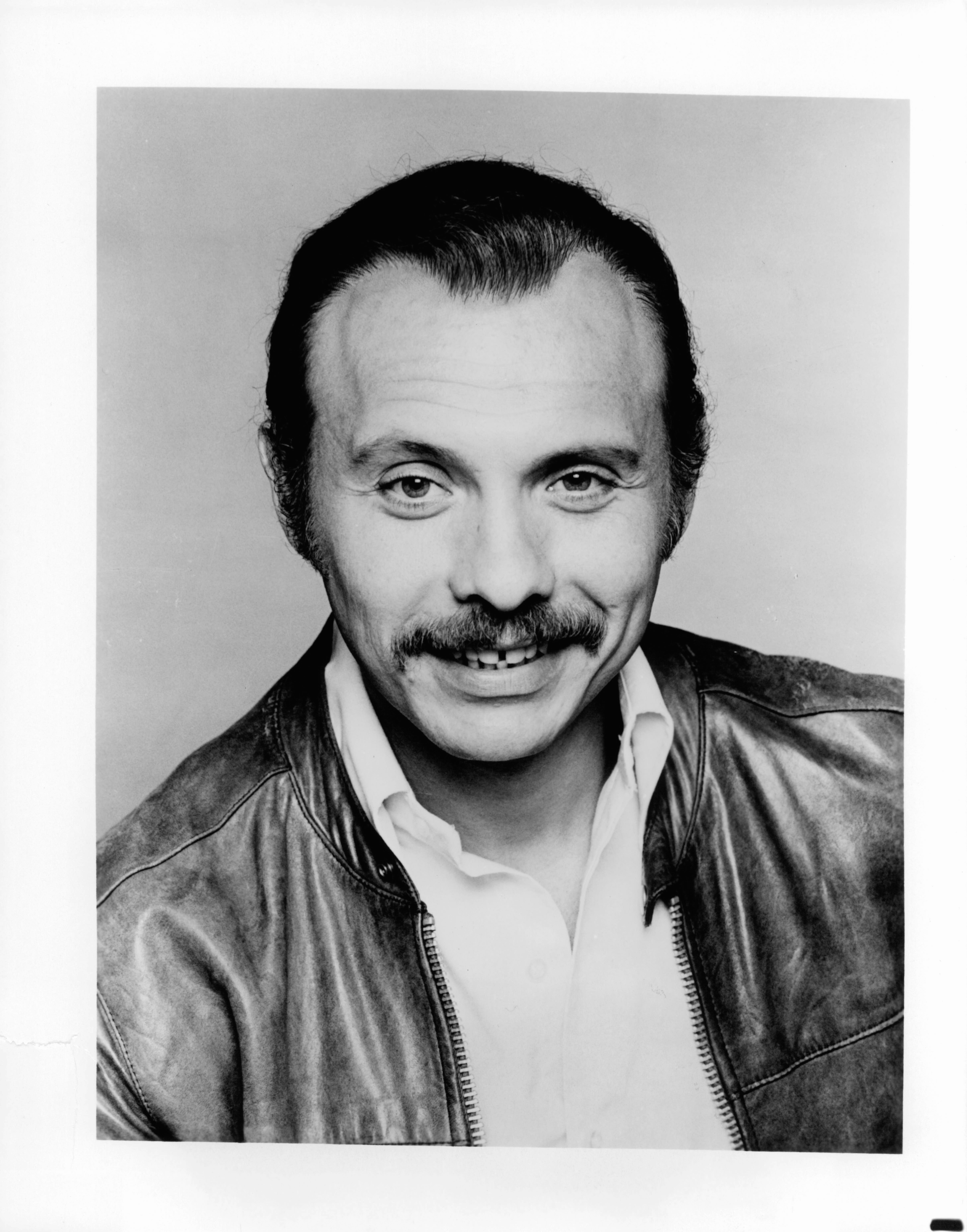 Person in a leather jacket and button-up shirt, smiling at the camera