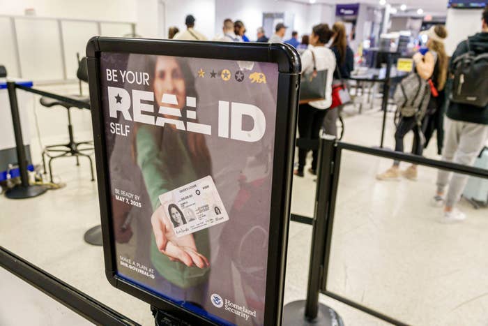 A sign at an airport security checkpoint promoting the Real ID with a woman holding up an ID card, stating "Be your REAL ID self."