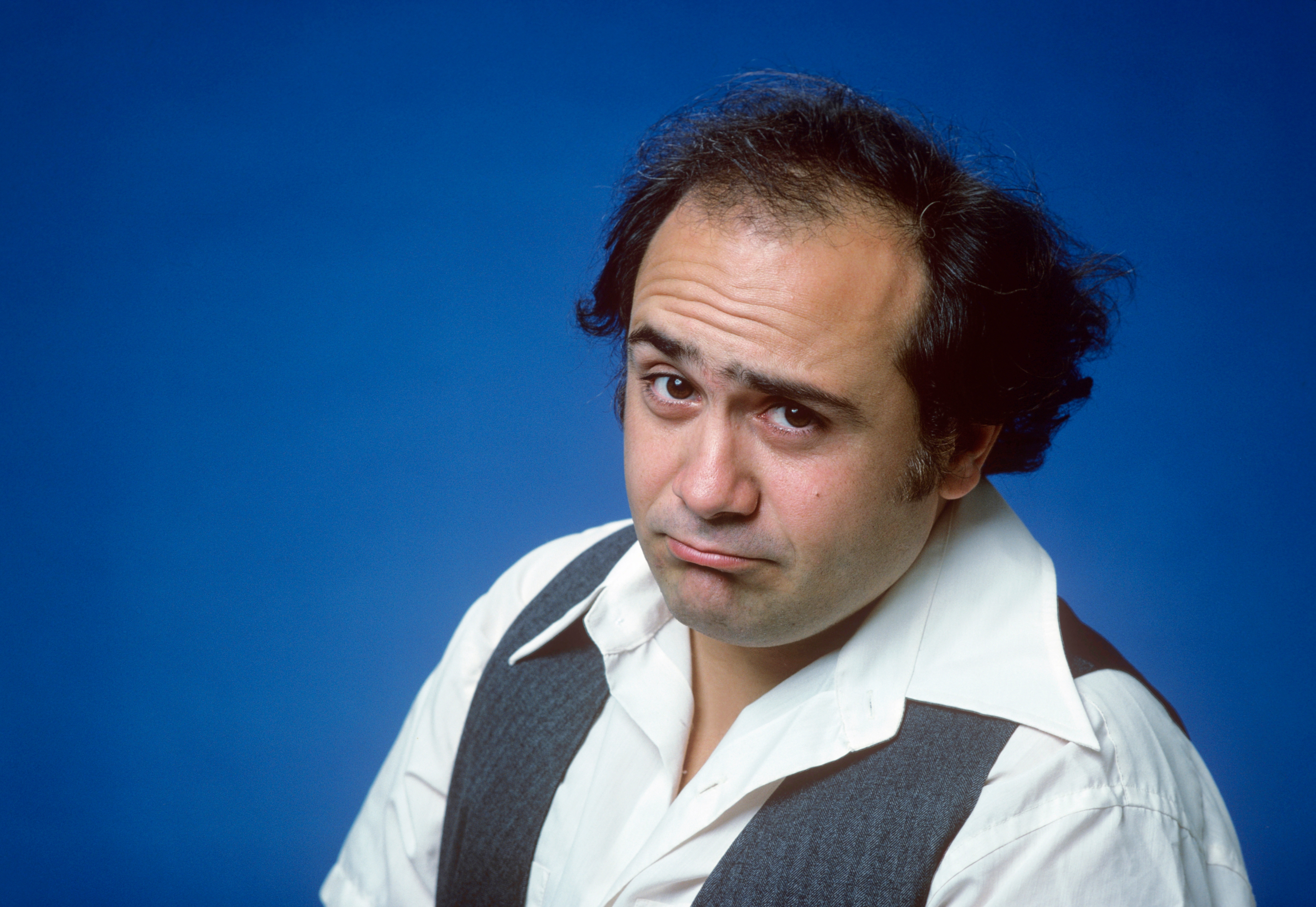 Actor with a quizzical expression, wearing a white shirt and gray vest against a plain background