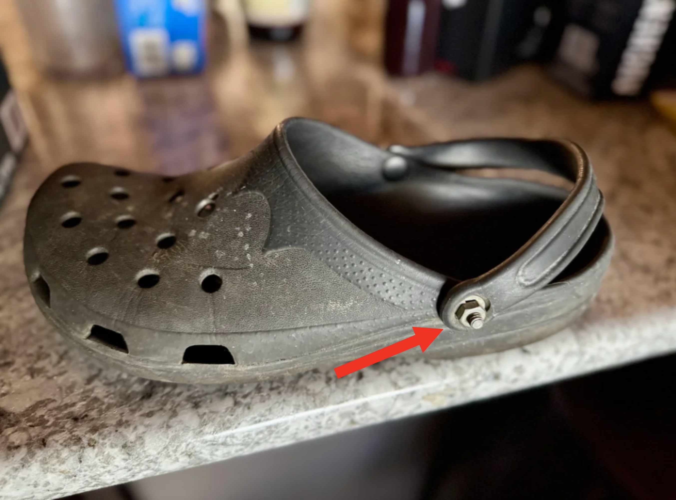 A single worn-out clog-style shoe sits on a countertop, featuring a strap and ventilation holes