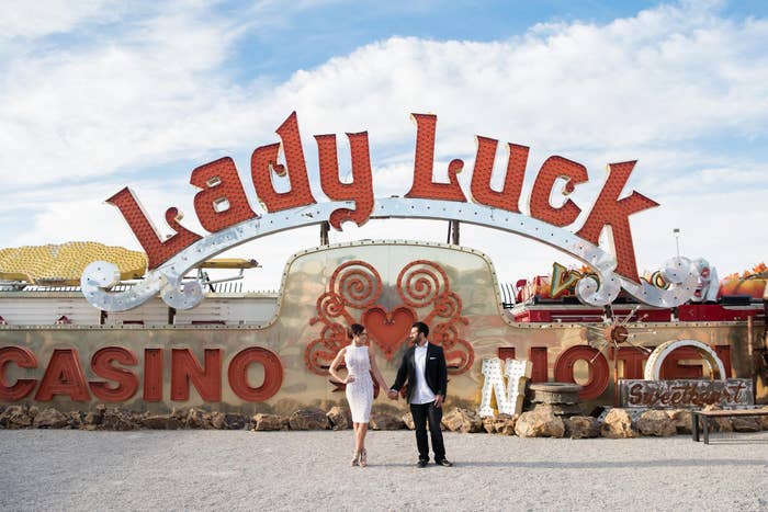 Two individuals stand in front of a vintage "Lady Luck Casino" sign, posing together with a retro theme