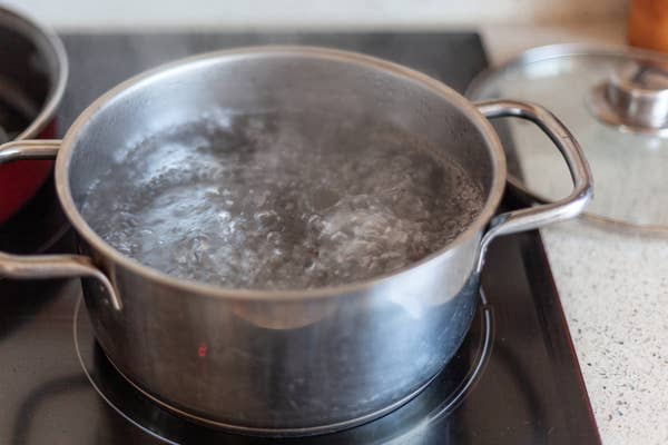 A pot of water boiling on a stovetop, with steam rising, indicating cooking in progress