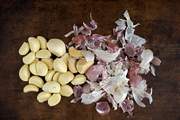 Peeled and unpeeled garlic cloves are placed side by side on a wooden surface