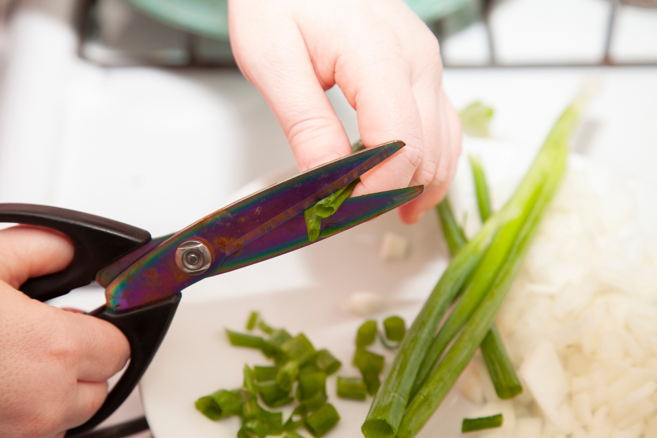 Scissors cutting green onions over a plate with chopped onions and green peppers