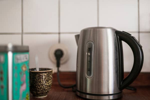 Electric kettle on a wooden kitchen counter next to a patterned mug and a plugged-in outlet