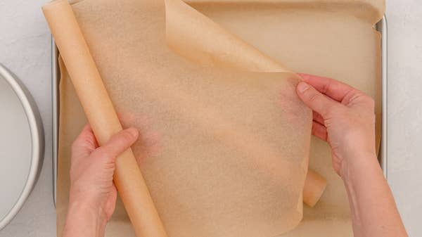 Hands placing parchment paper on a baking sheet