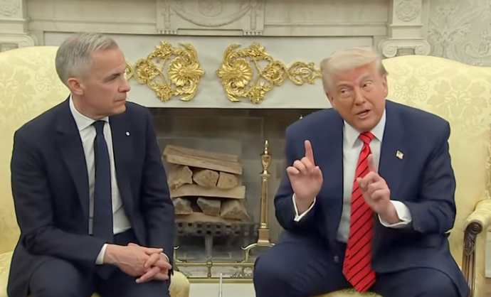 Two men seated at a formal meeting. The man on the right gestures while speaking, and both wear suits. A decorative fireplace is in the background