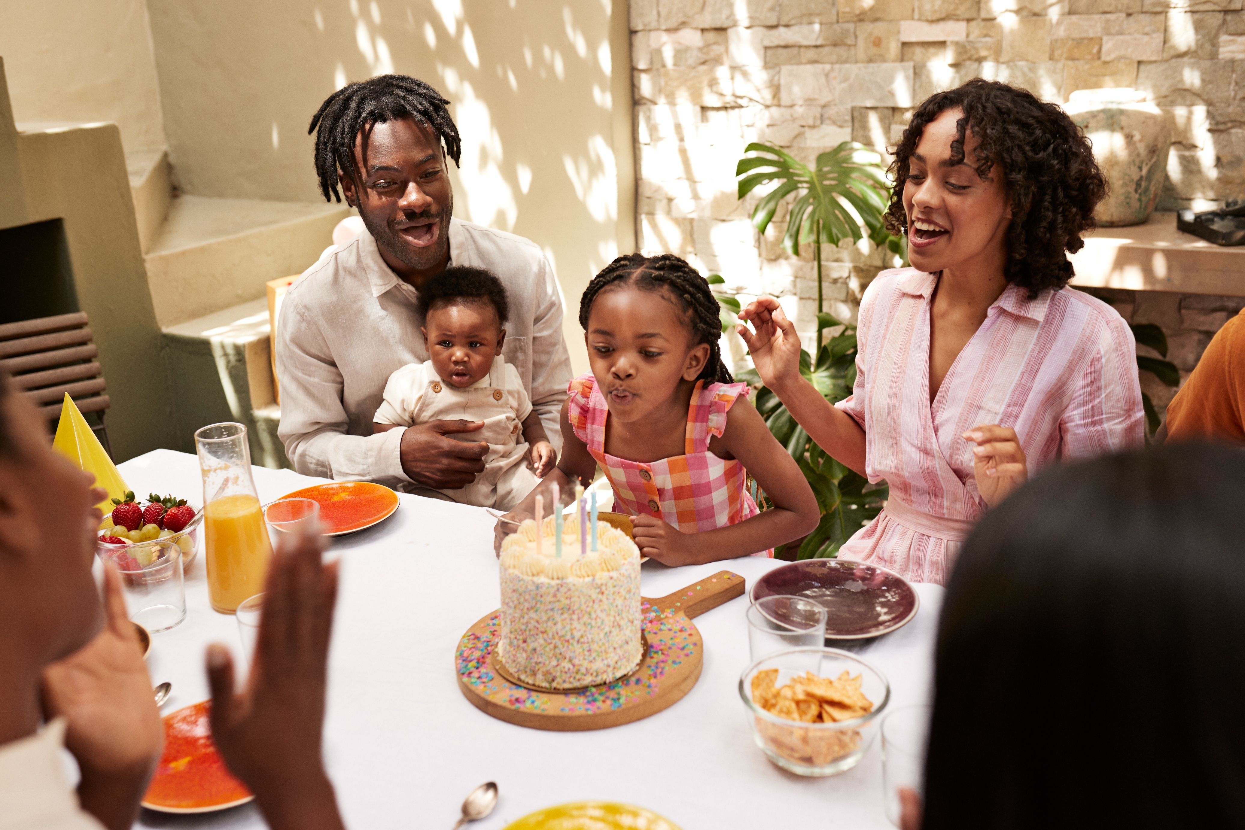 Familien feirer ved et bord; Barnet blåser ut lys på en kake mens andre smiler og klapper