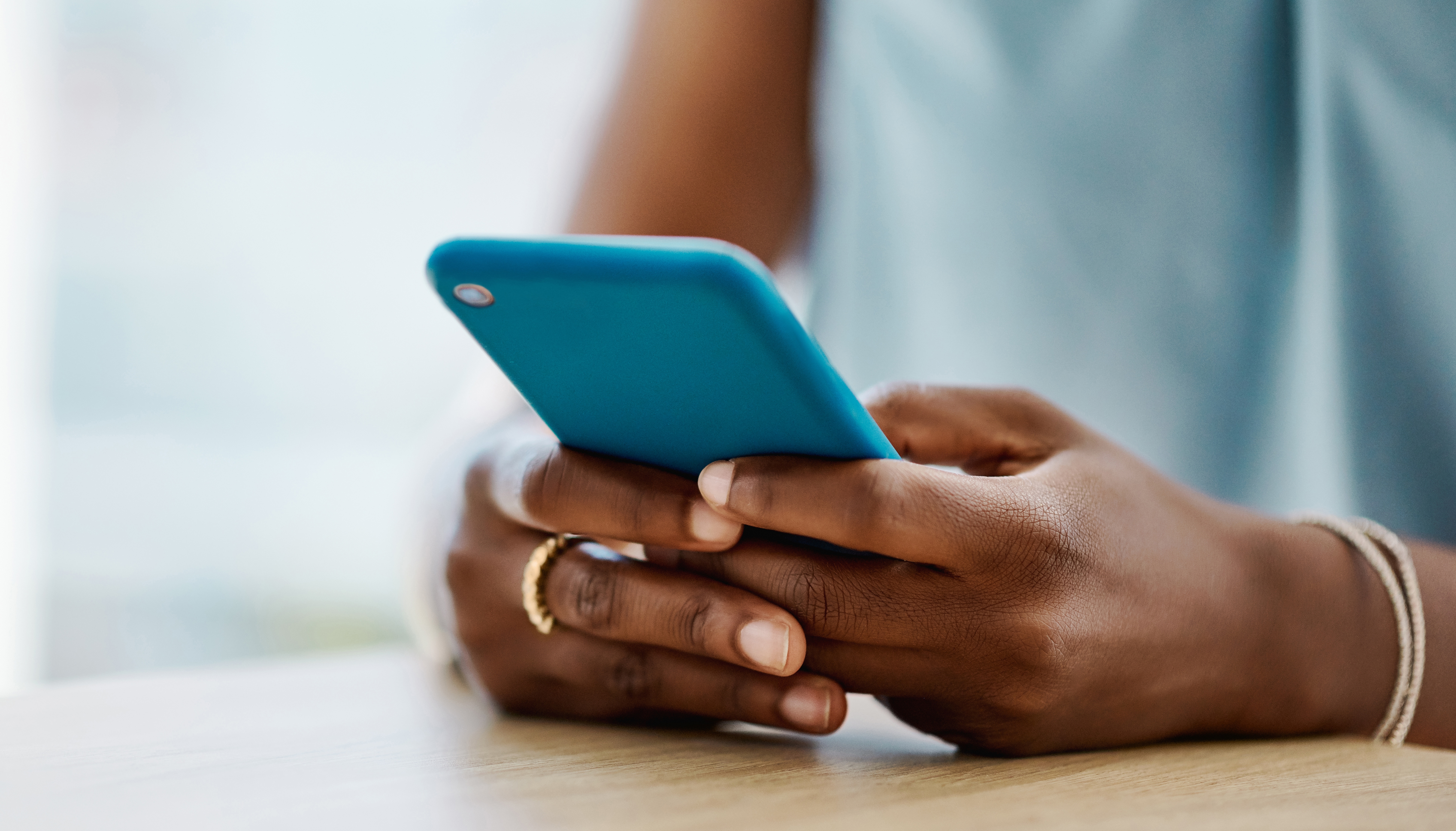 Person sitting at a table, holding a smartphone, focusing on the screen.