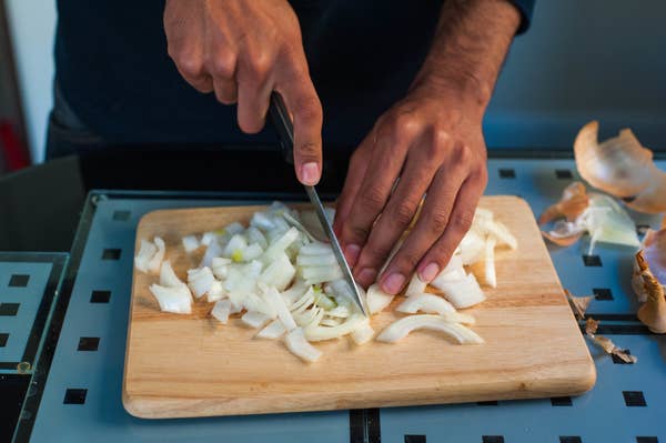 Person chopping onions on a wooden cutting board, preparing ingredients for cooking