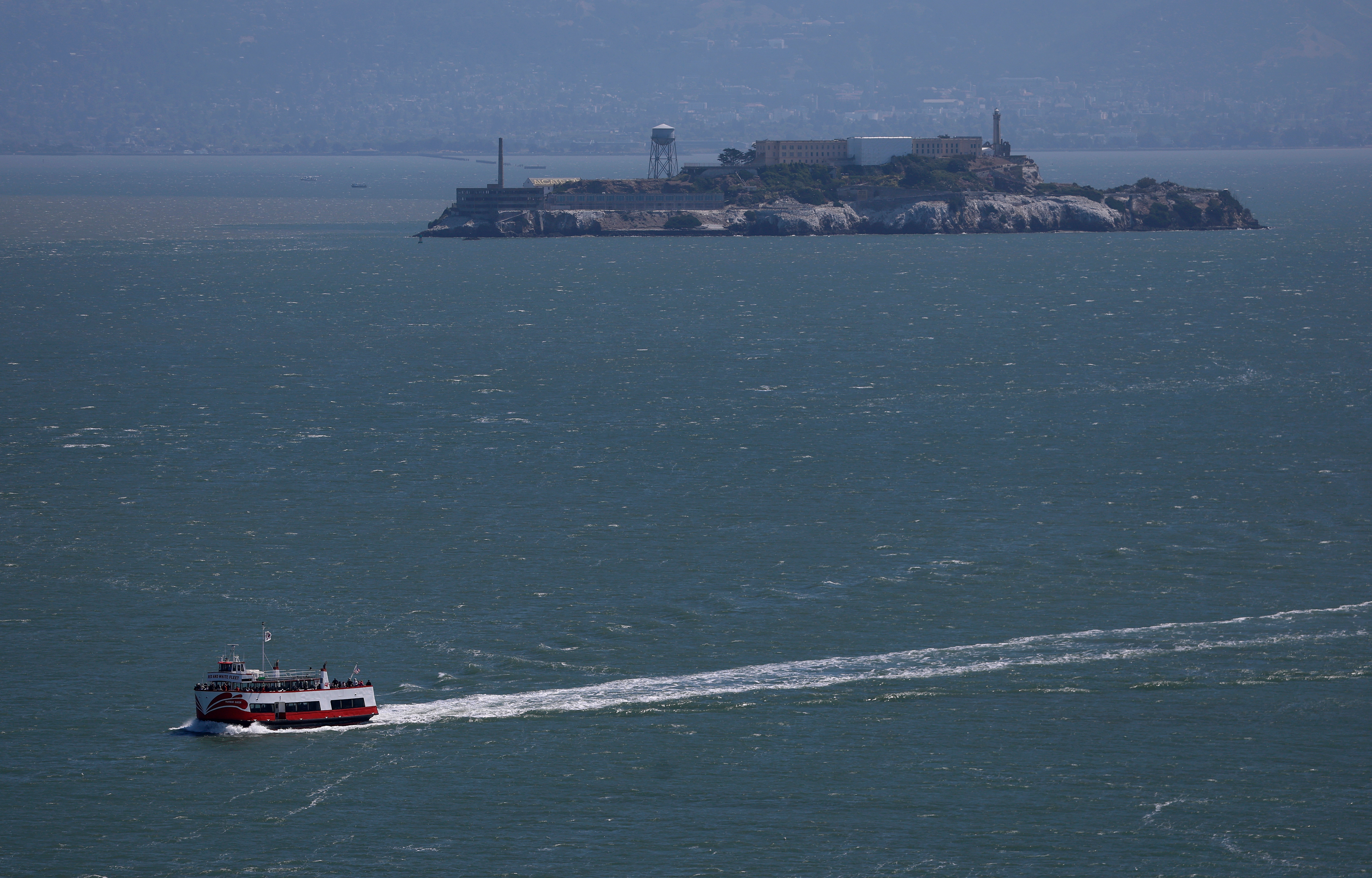 A boat sails toward Alcatraz Island with its historic prison against a foggy backdrop, seen from a distance