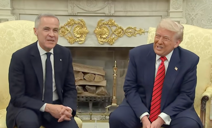 Two people sitting in formal suits, smiling in a room with an ornate fireplace behind them